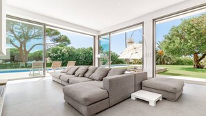 Una sala de estar moderna con un sofá seccional, una mesa de centro y ventanas amplias que ofrecen vista a una piscina y jardín.