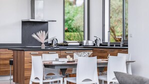 Una cocina moderna con una isla central, sillas blancas y ventanas amplias que dan a zonas verdes.