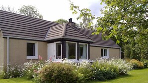 A single-story house with a sloped roof, a front porch, and a garden with various plants and flowers.
