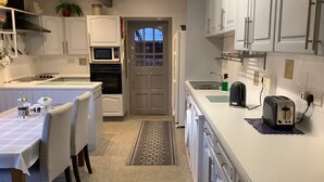 A modern kitchen with white cabinets, a microwave, a refrigerator, and a toaster. There is a dining area with a table and chairs.