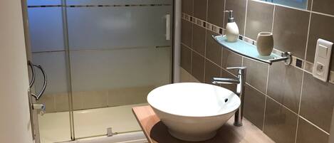 Un baño moderno con ducha de vidrio, un lavamanos blanco y un espejo sobre él.