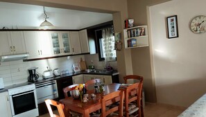 Una cocina con armarios blancos, una mesa de comedor con sillas, una cafetera y un reloj en la pared.