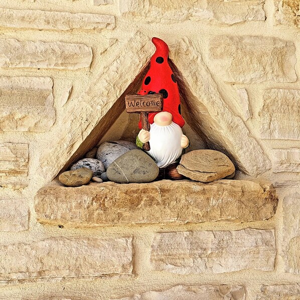 A gnome figurine sitting on a stone ledge with a 'Welcome' sign above it, set against a stone wall. - Villa Elia is situated in a quiet area, surrounded by olive trees with a private (Πιτσίδια)