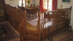 A dining area with a wooden table, chairs, and a bench. There is a staircase with a wooden railing leading to another level.