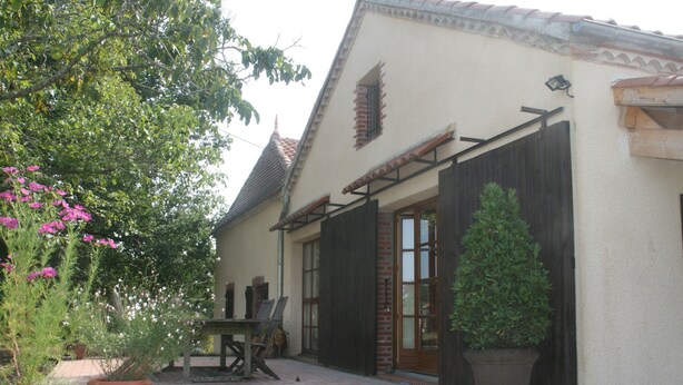 A house with a tiled patio, a wooden table, and potted plants.