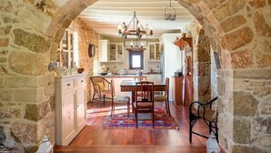 A rustic kitchen with stone walls, wooden flooring, a central island, and a chandelier. - The old cheese hut Su (Ζου)