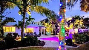 Un espacio exterior bien iluminado con piscina, sillas de descanso y una palmera decorada con luces de colores.