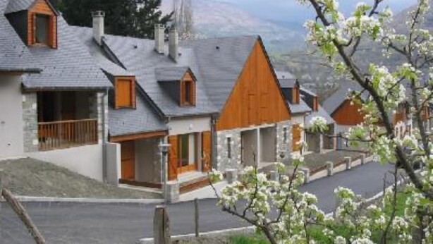 A row of traditional houses with pitched roofs and wooden accents, set against a backdrop of mountains and blooming trees. - chalet - SAINT LARY SOULAN (Vignec) (VIGNEC)