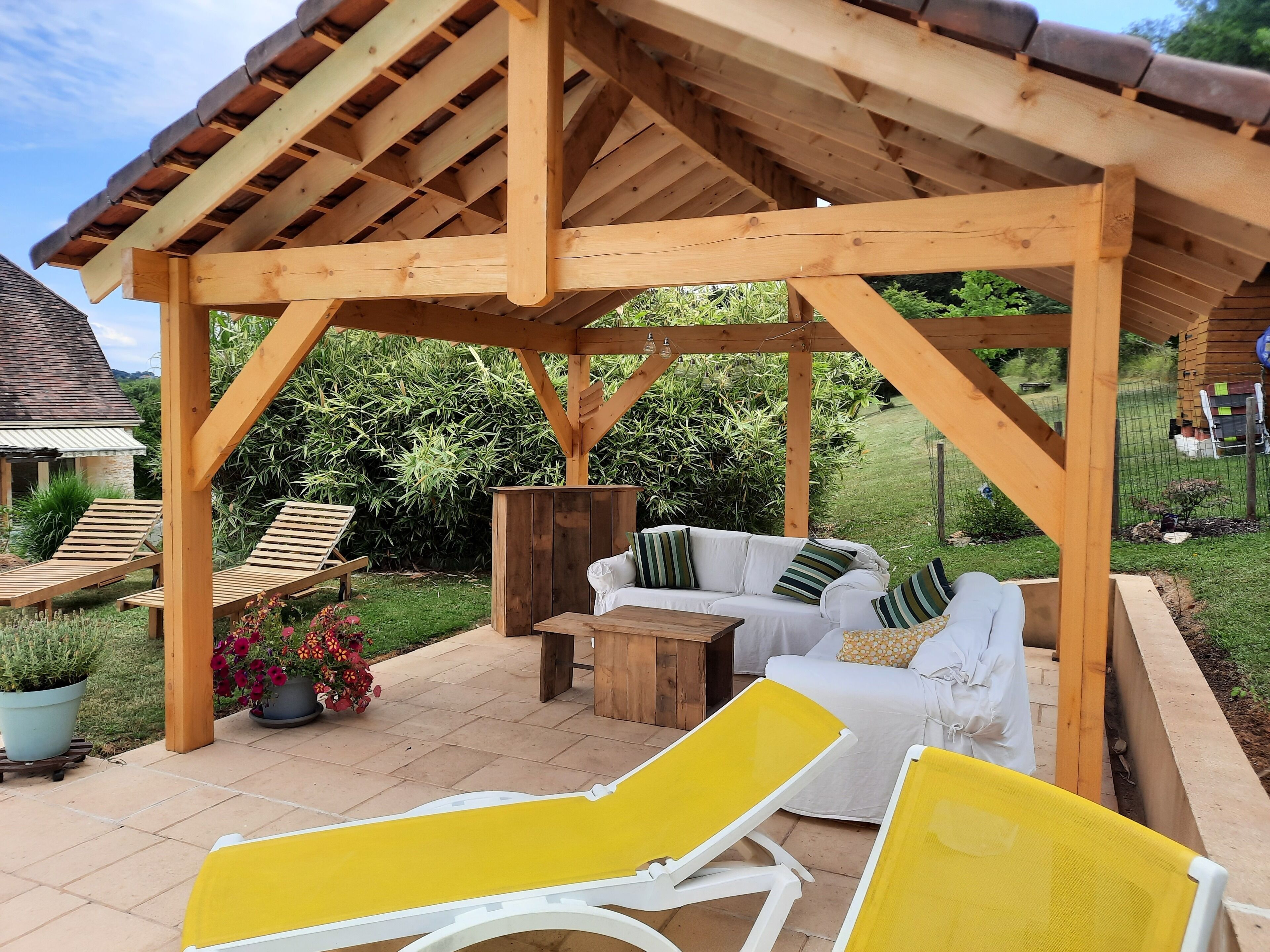 Uma pérgola de madeira com área de estar acolchoada, incluindo um sofá e duas poltronas.