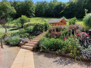 Ein Garten mit einer Holzpergola, einem Kiesweg und verschiedenen Pflanzen.