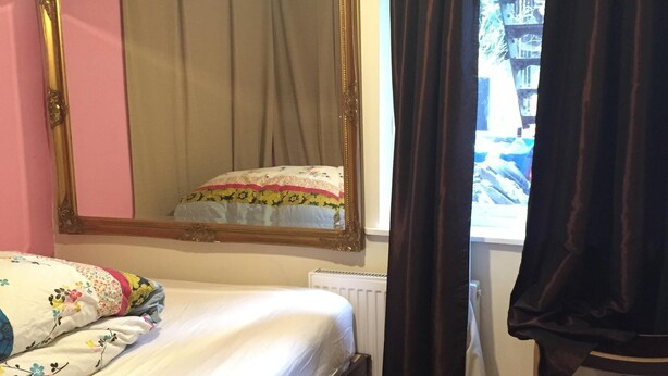 Une chambre à coucher avec un lit, un grand miroir, une fenêtre avec des rideaux et un radiateur.