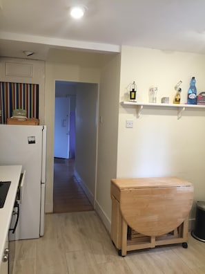 Kitchen area with refrigerator, bench, and shelving for storage.