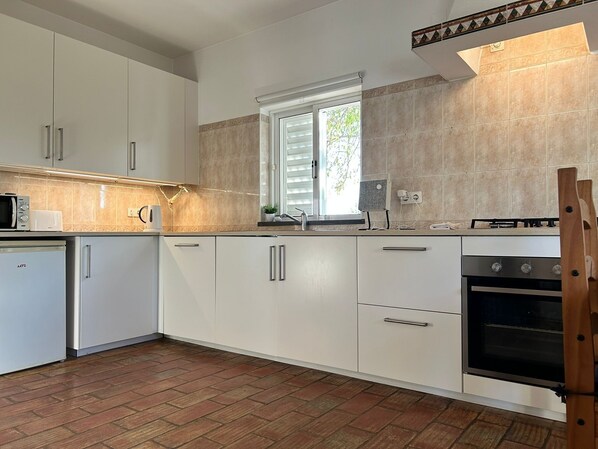 Une cuisine moderne avec des meubles blancs, un four encastré et une fenêtre équipée de stores.
