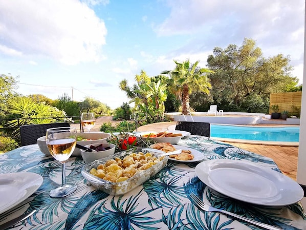 An outdoor dining area with a pool, surrounded by greenery and palm trees. - Portugal Private Villa with private pool rural quiet tranquil setting (moncaropacho)