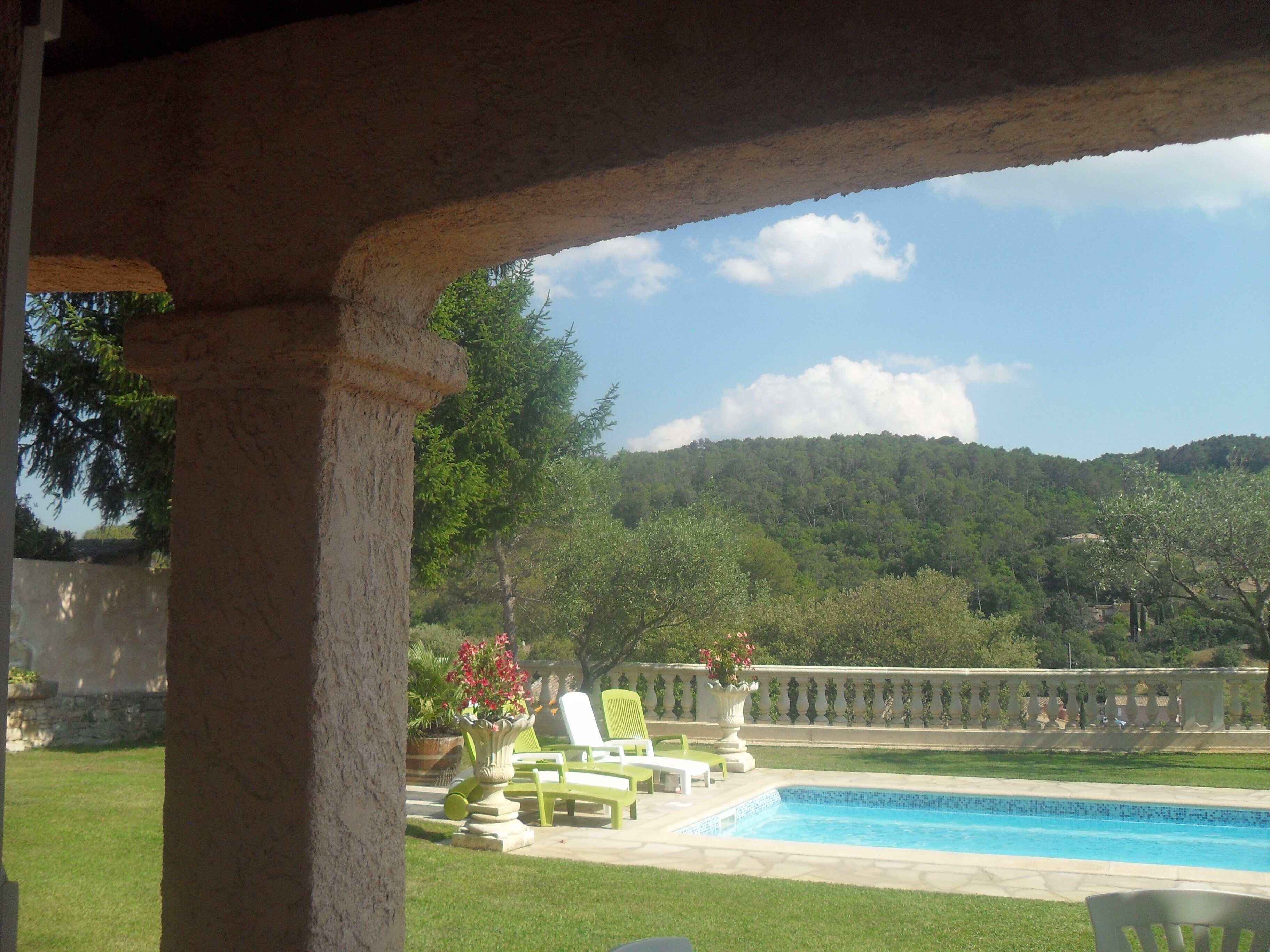 Uma área de piscina com cadeiras de descanso verdes e vista para uma colina arborizada.