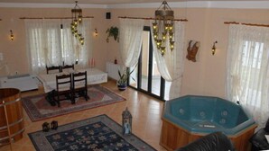 Ett rymligt vardagsrum med en stor blå jacuzzi, ett matbord med stolar, en trätunna och en mönstrad matta.