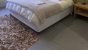 A neatly made bed with a headboard, a bedside table with a lamp, and a window with curtains.