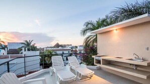 A rooftop terrace with white lounge chairs, a small sink, and a view of the cityscape during sunset. - Swimming Pool, Rooftop Terrace, 4 Blocks from Ocean (Cozumel)