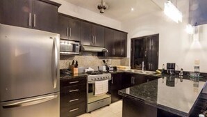 A modern kitchen with dark cabinetry, stainless steel appliances, and a granite countertop. - Swimming Pool, Rooftop Terrace, 4 Blocks from Ocean (Cozumel)