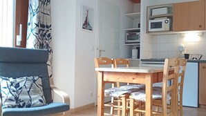 Ett kompakt kök med träskåp, en mikrovågsugn och en matplats med ett bord och stolar.
