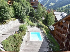 Um deck de madeira com piscina, rodeado por vegetação e vista para as montanhas.