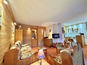 Um interior de madeira aconchegante com um conjunto de sofás, uma televisão e uma área de cozinha.