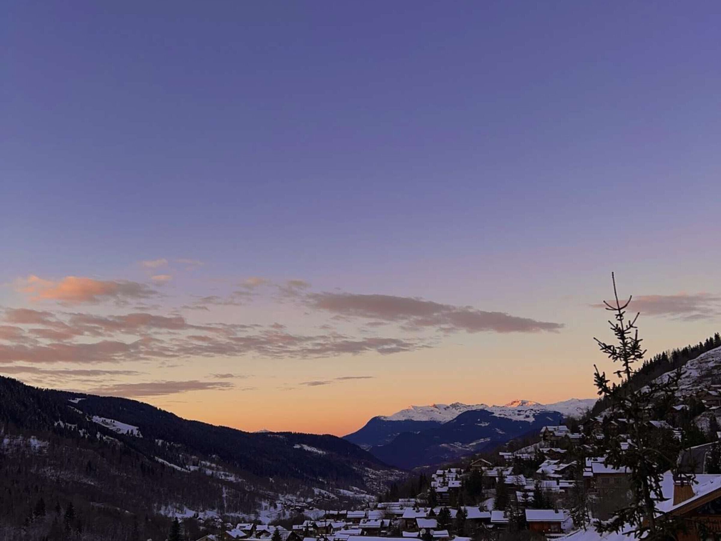 Ein verschneites Dorf mit Häusern und Bergen im Hintergrund.