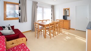 A room with a wooden dining table and chairs, a red sofa, a small wooden cabinet, and a television. - Balcons G 025 - PARC NAT. VANOISE appart. 8 pers. (Val Cenis)