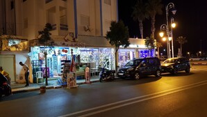 A street scene at night with a brightly lit shop and parked cars. - Modern flat with sea view in martil (Martil)