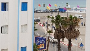 A coastal view with a building, palm trees, and a beach with colorful flags. - Modern flat with sea view in martil (Martil)