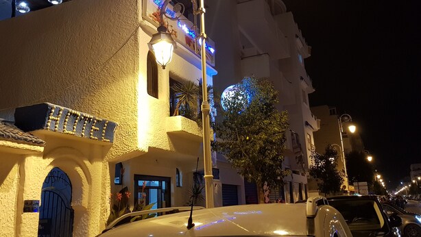 A building with a textured facade, a balcony with a railing, and a sign with illuminated text. - Modern flat with sea view in martil (Martil)