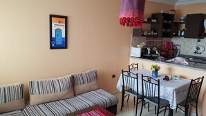 A living room with a striped sofa, a dining table with chairs, and a kitchen area with cabinets and appliances. - Modern flat with sea view in martil (Martil)