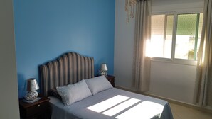A bedroom with a bed, a nightstand, a lamp, and a window with curtains. - Modern flat with sea view in martil (Martil)