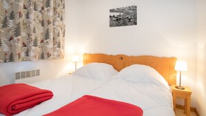Ein Hotelzimmer mit hölzernem Kopfteil, weißer Bettwäsche, roten Decken, zwei Nachttischlampen, einem Fenster mit Vorhängen und einem Wandbild.