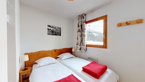 Une chambre à coucher avec une tête de lit en bois, un lit avec une literie blanche et une serviette rouge, une table de chevet avec une lampe, une fenêtre avec des rideaux et une étagère murale décorative.