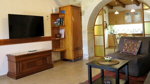 Sala de estar com televisão de tela plana, móveis de madeira e vista para a cozinha através de um arco.