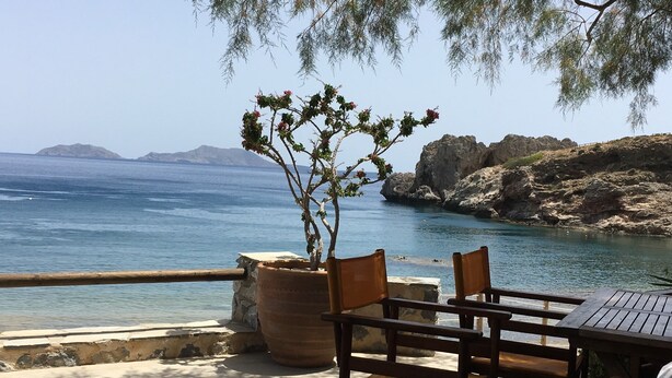 Um terraço à beira-mar com mesa e cadeiras, com vista para o mar e a costa rochosa.