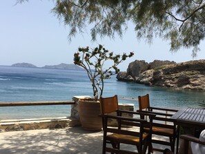 A seaside terrace with a table and chairs, overlooking the sea and rocky coastline.