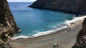 Uma praia rochosa com águas azuis cristalinas, algumas pessoas e uma tenda montada.
