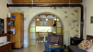 Uma sala de estar acolhedora com um sofá, uma mesa de centro e um suporte para TV. Cozinha visível através de uma porta arqueada.
