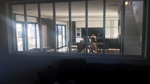 A modern living room with a large window overlooking a kitchen and dining area.