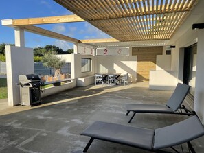 An outdoor patio with a grill, lounge chairs, and a table with chairs. - Modern house on La Baule international golf course (Saint-André-Des-Eaux)