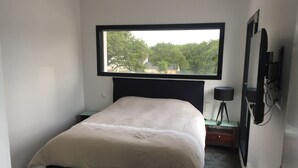 A bedroom with a bed, a nightstand, a lamp, and a window with a view of trees.