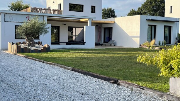 A modern two-story house with a covered patio, a small garden, and a gravel driveway.