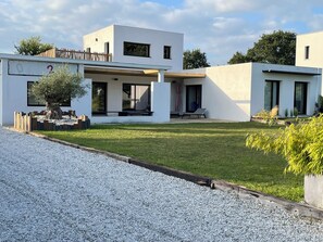 A modern two-story house with a covered patio, a small garden, and a gravel driveway.