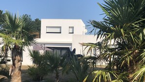 A modern white building with a flat roof, surrounded by palm trees and a well-maintained garden.