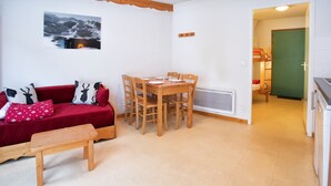 Una sala acogedora con un sofá rojo, una mesa de comedor de madera y un pequeño banco de madera.
