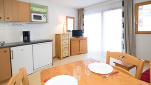 Una cocina con microondas, cafetera y armarios de madera. Hay una mesa de comedor con sillas y un televisor sobre un mueble.
