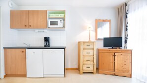 Una cocina compacta con armarios de madera, microondas, cafetera, lavavajillas, un armario con cajones y un televisor sobre un mueble de madera.