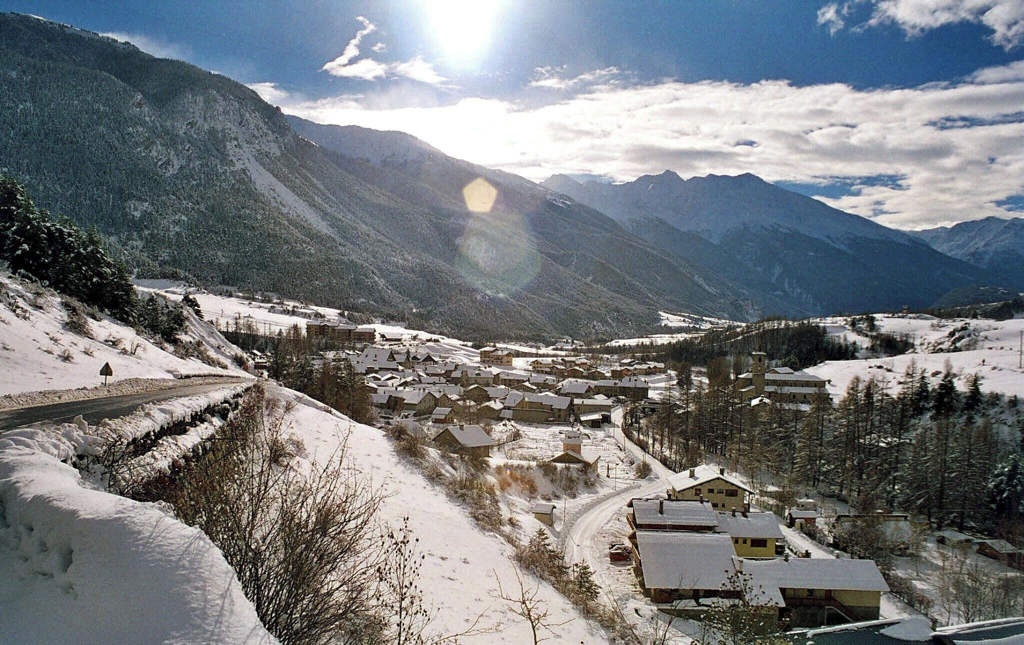 Un pueblo cubierto de nieve con casas y una carretera, rodeado de montañas.